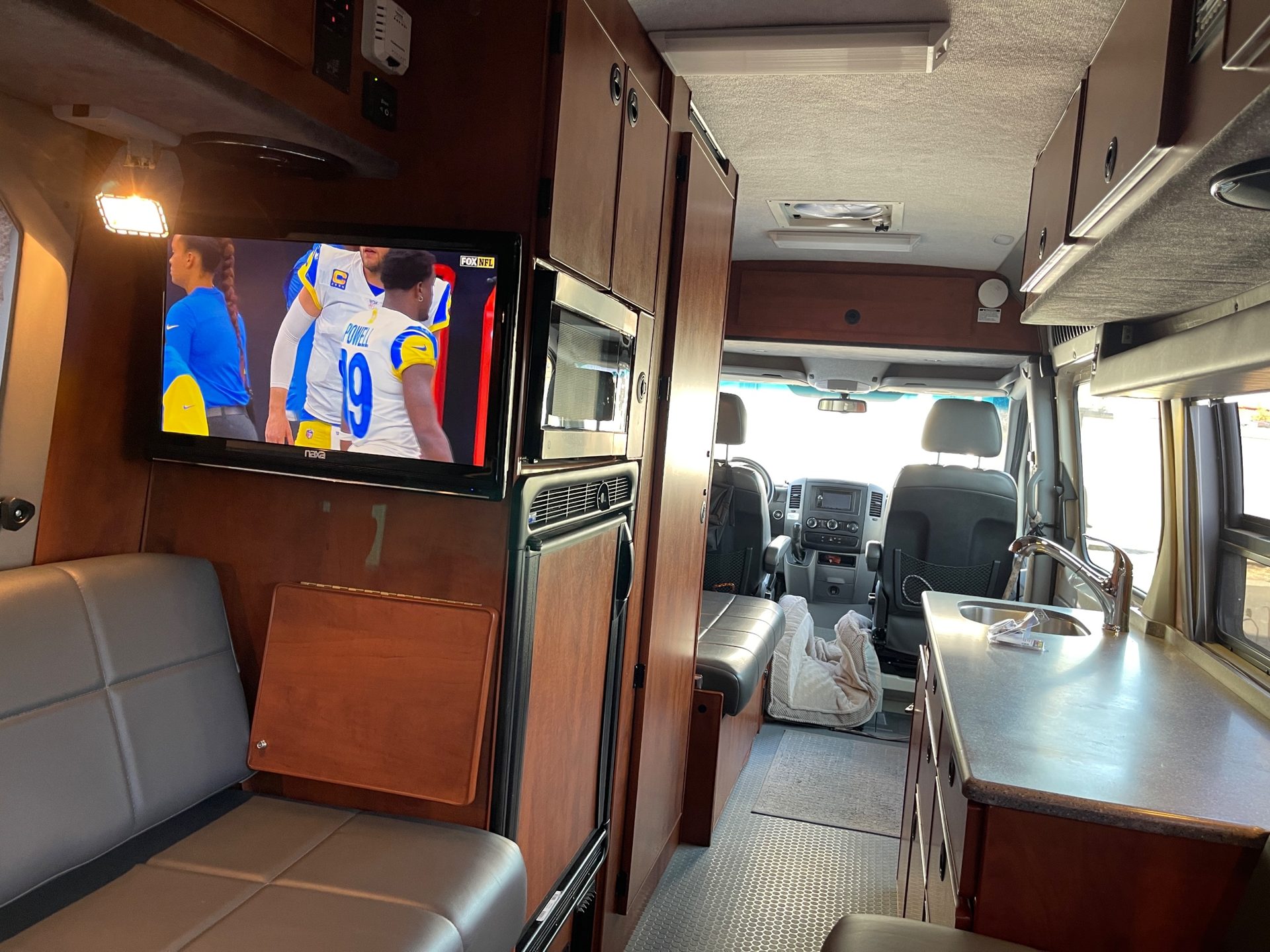 Inside the author's 2013 Sportsmobile looking toward the cab: wood cabinetry, a wall-mounted TV, microwave and refrigerator, and the galley counter
