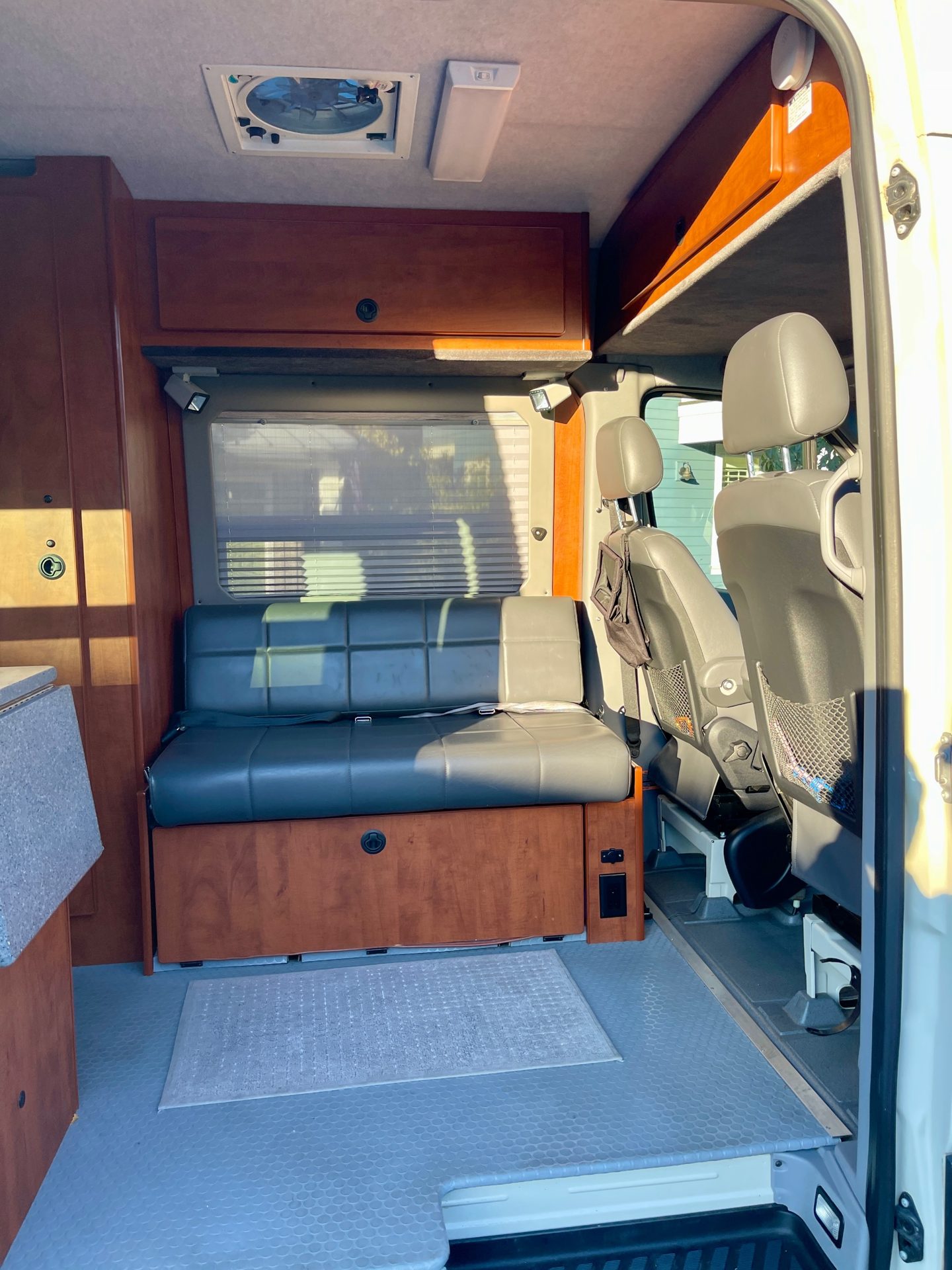 The front lounge of the author's 2013 Sportsmobile: a gray bench seat facing the swiveling cab seats, with a ceiling fan above